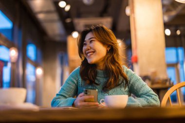 Kahve dükkanında cep telefonu kullanan genç bir kadın.