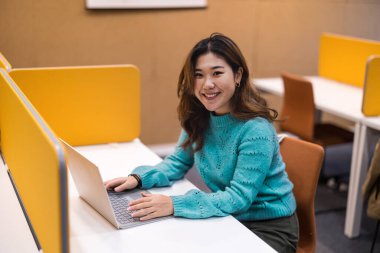 Kütüphanede dizüstü bilgisayarda çalışan bir kız öğrenci.