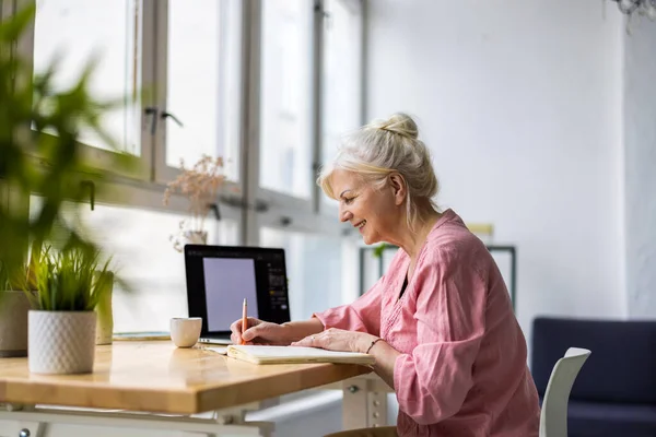Lächelnde Reife Geschäftsfrau Schreibt Notizbuch Während Sie Büro Tisch Sitzt — Stockfoto