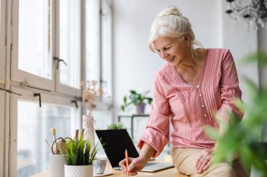 Masada otururken deftere yazan gülümseyen olgun bir iş kadını.