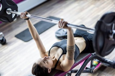 Genç bir kadın spor salonunda halterle çalışıyor. 