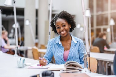 Genç siyahi kadın kütüphanede deftere yazıyor.