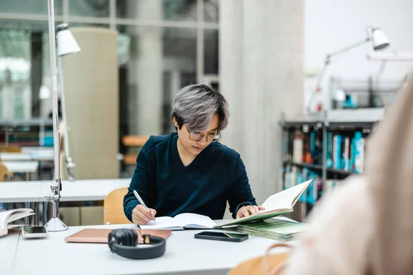 Asyalı Öğrenci Kütüphanedeki Masada Deftere Yazı Yazıyor — Stok fotoğraf