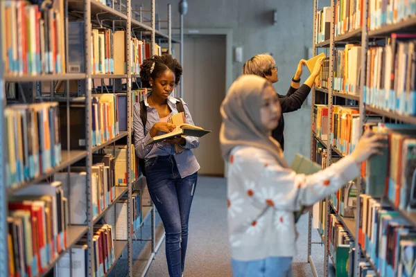 Többnemzetiségű Diákok Csoportja Könyvespolcról Választ Könyveket Egy Könyvtárban — Stock Fotó