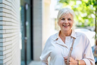 Şehirde dikilen mutlu yaşlı kadının portresi.