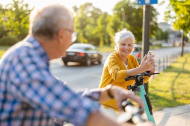 Şehirde elektrikli scooter kullanan yaşlı bir çift.