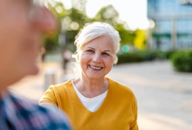 Güneşli bir günde şehir sokağında dikilen mutlu yaşlı çiftin portresi.