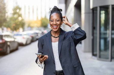 Şehirde cep telefonu olan gülümseyen bir kadının portresi.