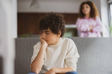 Annesi ona bakarken kanepede oturan üzgün çocuk.