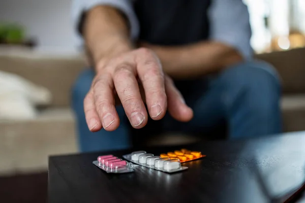 Close-up of man taking pills on sofa at home in the living room