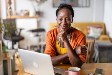 Evde dizüstü bilgisayarda çalışan gülümseyen kadın.