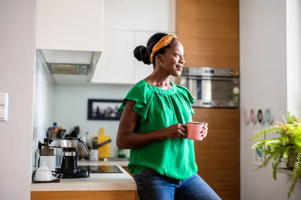 一个微笑的成熟女人站在厨房喝咖啡的画像 免版税图库照片