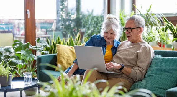 Seniorenpaar Benutzt Laptop Während Hause Auf Sofa Wohnzimmer Sitzt Stockfoto
