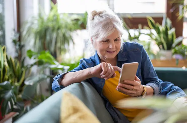Usmívající Starší Žena Pomocí Chytrého Telefonu Zatímco Sedí Pohovce Doma Stock Obrázky