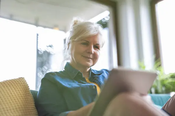 Reife Frau Nutzt Digitales Tablet Während Sie Hause Auf Dem lizenzfreie Stockbilder