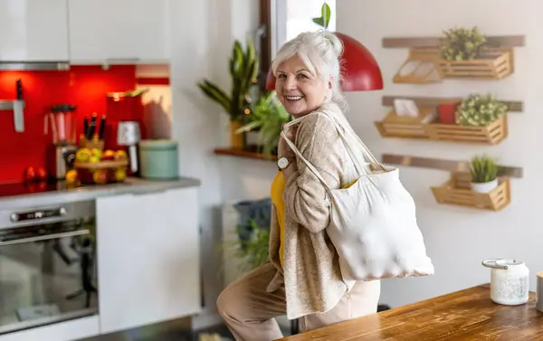 Seniorin Hält Mehrwegtasche Mit Lebensmitteln Küche lizenzfreie Stockbilder