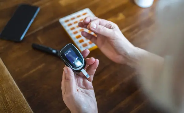 Elderly Woman Checking Her Blood Sugar Level While Sitting Home Stock Photo