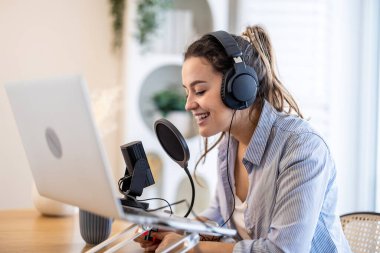 Masada oturmuş mikrofona konuşan ve podcast kaydeden kulaklık takan bir kadın.
