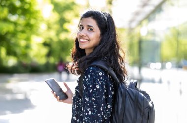 Şehirde akıllı telefonunu kullanan gülümseyen genç bir kadın.