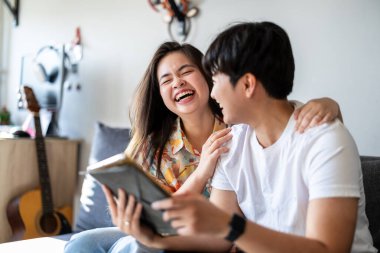 Mutlu genç çift evdeki kanepede dijital tablet kullanıyor.