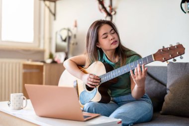 Evde gitar çalan genç bir kadın.