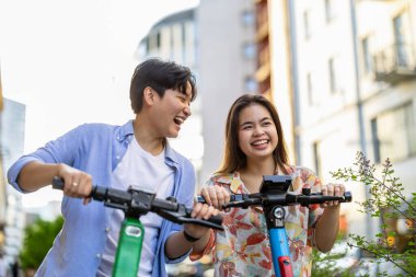 Şehirde elektrikli scooter kullanan gülümseyen genç bir çift.