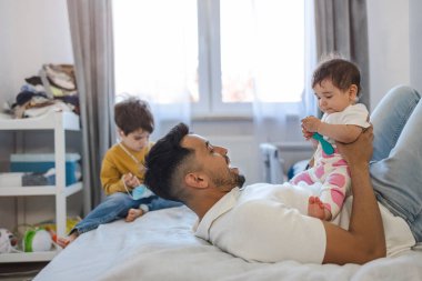 Genç baba evde iki küçük çocuğuyla oynuyor.