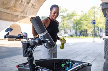 Woman going to the gym packing sports equipment into a cargo bike clipart