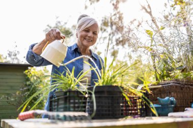 Bahçesinde bitkileri sulayan olgun bir kadın.