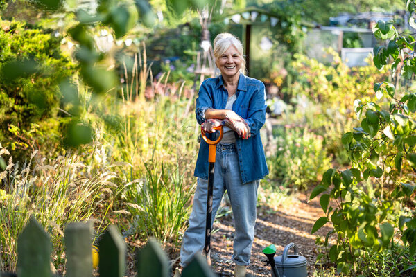 Старшая женщина работает в своем саду в солнечный день