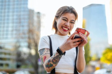 Şehirde cep telefonu kullanan mutlu genç bir kadın.