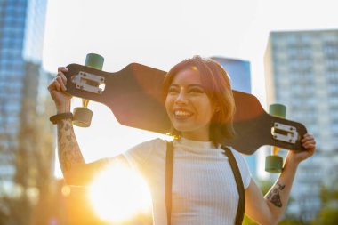 Şehirde kaykaylı gülümseyen genç bir kadının portresi.