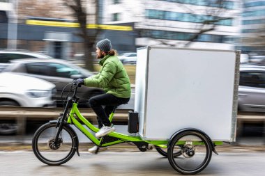 Bisikletli kurye şehirde kargo motosikletiyle paket teslimatı yapıyor.