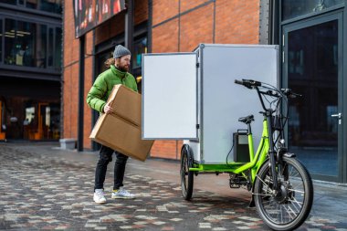 Bisikletli kurye şehirde kargo motosikletiyle paket teslimatı yapıyor.