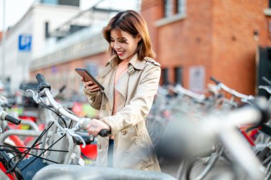 Şehirdeki bisiklet kiralama istasyonundan bisikletli genç bir kadın.