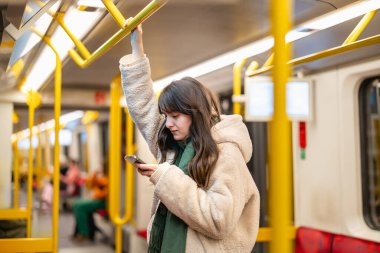 Metrodayken telefonunu kullanan genç bir kadın.
