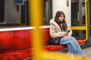 Metrodayken telefonunu kullanan genç bir kadın.