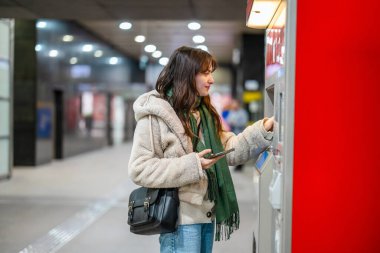 Bir makineden metro bileti alan genç bir kadın.