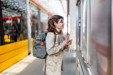 Tren istasyonunda cep telefonu kullanan gülümseyen genç bir kadının portresi
