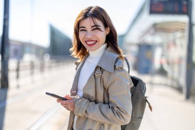 Tren istasyonunda cep telefonu kullanan gülümseyen genç bir kadının portresi