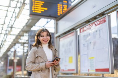 Tren istasyonunda cep telefonu kullanan gülümseyen genç bir kadının portresi