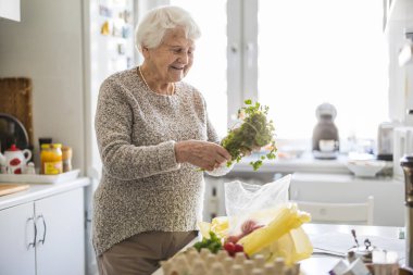 Mutfakta kıdemli bir kadın, taze sebze siparişini kontrol ediyor.