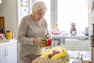 Mutfakta kıdemli bir kadın, taze sebze siparişini kontrol ediyor.