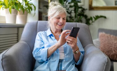 Evde cep telefonu kullanan yaşlı bir kadın.