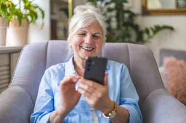 Evde cep telefonu kullanan yaşlı bir kadın.