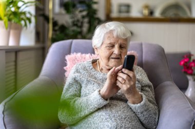 Evde cep telefonu kullanan yaşlı bir kadın.