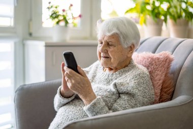 Evde cep telefonu kullanan yaşlı bir kadın.