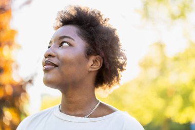 Güneşli bir günde parkta gülümseyen genç bir kadının portresi.
