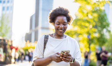 Şehirde cep telefonu kullanan gülümseyen genç bir kadının portresi
