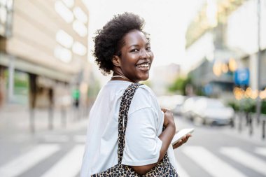 Şehirde cep telefonu kullanan gülümseyen genç bir kadının portresi